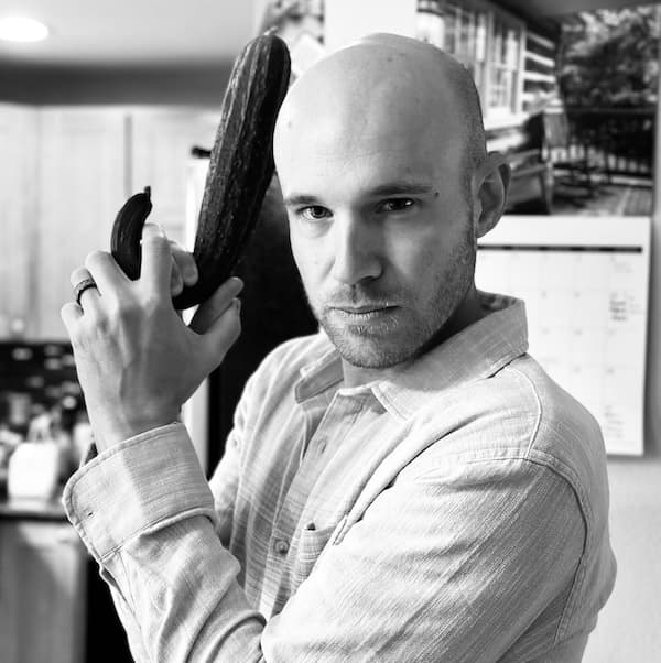 Andrew holding a cucumber like a weapon, with a noir filter